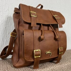 Mochila de silueta estructurada con doble solapa, correas decorativas con hebillas metálicas doradas, cierre de cordón ajustable y herraje de firma en relieve.