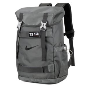 Mochila deportiva Nike en color gris con el logotipo "Swoosh" en negro, cierre superior tipo tapa con dos hebillas blancas, correas de compresión y diseño técnico de alta resistencia.