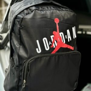Morral deportivo marca Jordan con el logo "Jumpman" en rojo y el nombre de la marca en letras blancas y negras, disponible en color negro sólido y blanco con bolsillo frontal negro.