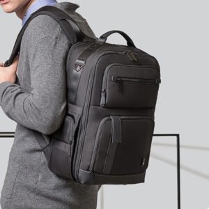 Morral ejecutivo de diseño estructurado con múltiples compartimentos frontales con cremallera, asa superior reforzada y correas ergonómicas, portado por un hombre con vestimenta casual-formal.