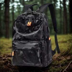Morral escolar o casual con estampado de camuflaje oscuro, cremalleras con tiradores en color naranja vibrante, bolsillos laterales y puerto de carga USB integrado.