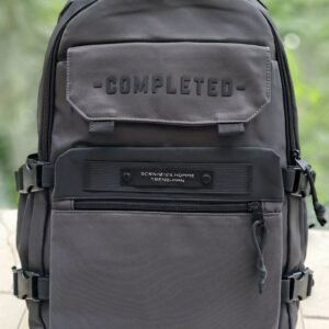 Morral gris oscuro de estilo técnico marca COMPLETED, con correas laterales de seguridad, compartimento frontal con etiqueta táctica y diseño ergonómico de alta resistencia.