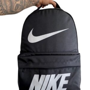 Morral deportivo de color negro con el logotipo de Nike en blanco grande impreso en la parte superior y el nombre de la marca en la parte inferior, sostenido por una mano, ideal para gimnasio o uso casual.